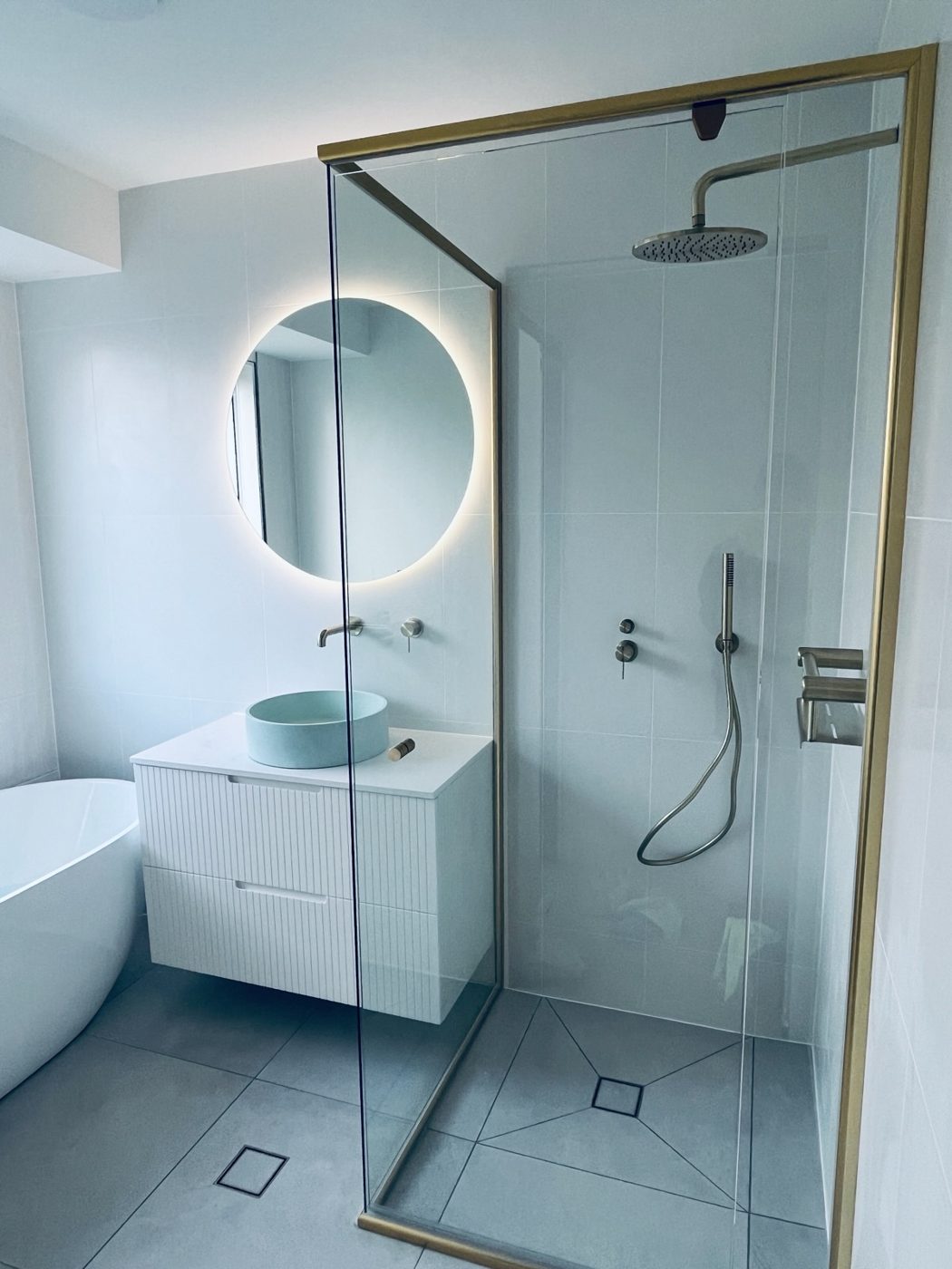 Renovated bathroom with brass-framed glass shower and round backlit mirror