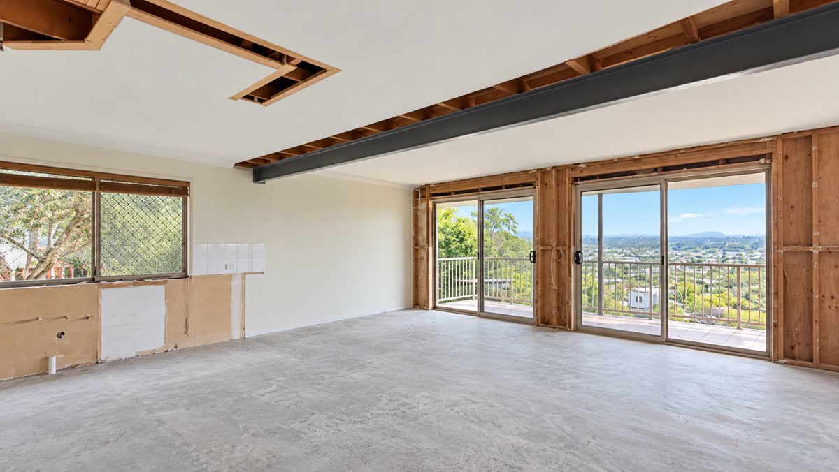 Stripped-out living area with exposed framing, steel beam and balcony doors before renovation